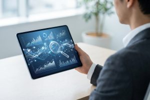 Vue de dos d'une personne tenant une tablette affichant des graphiques de données, une loupe et des connexions numériques bleues.