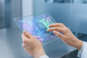 Mains manipulant une tablette transparente lumineuse. L'écran affiche des circuits, icônes de cadenas et la lettre A, évoquant l'IA et la sécurité.